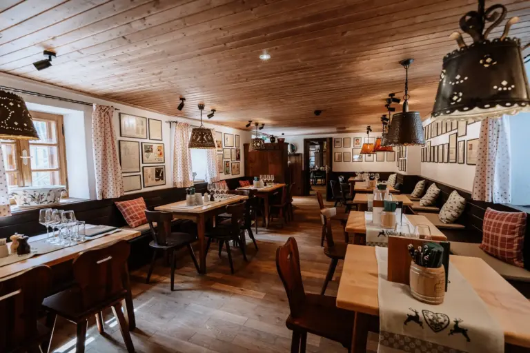 Ein gemütliches Restaurant mit Holzböden und -decken, die von Hängelampen warm beleuchtet werden. Die Tische sind mit Gläsern und Geschirr eingedeckt, und an den Wänden stehen gepolsterte Sitzbänke, die mit gerahmten Bildern dekoriert sind.