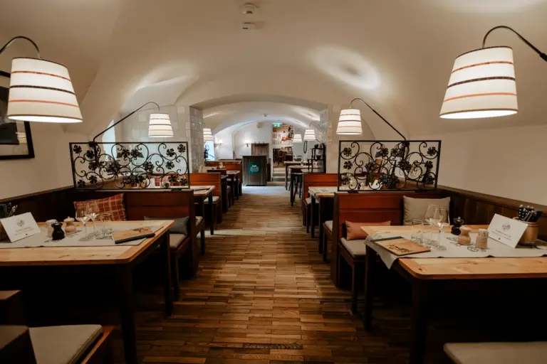 Ein gemütliches, warm beleuchtetes Restaurant mit Holzböden, Tischen und Stühlen, dekorativen Metallwänden und modernen Hängelampen, das zum Essen eingerichtet, aber derzeit leer ist.