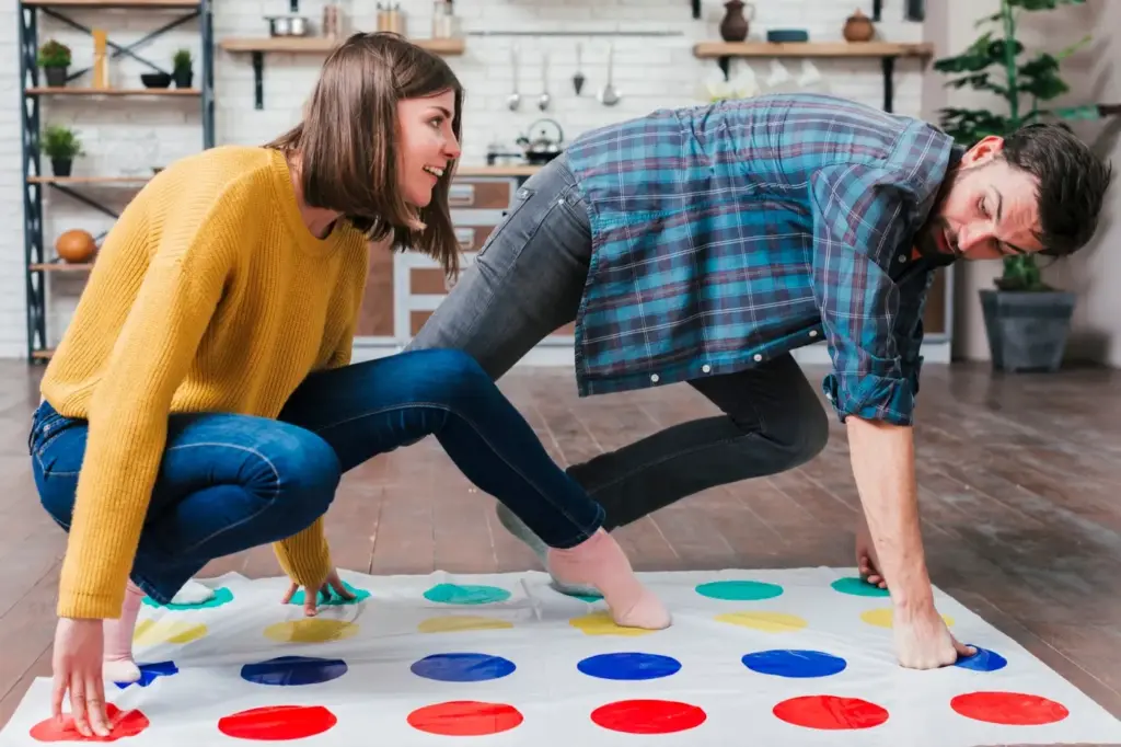 Zwei Personen spielen Twister auf einer Matte mit farbigen Kreisen in einem modernen Wohnzimmer, ähnlich wie bei einer spannenden Runde Wahrheit oder Pflicht Fragen. Einer trägt einen gelben Pullover, der andere ein kariertes Hemd - beide sind beschäftigt und balancieren auf Händen und Füßen.