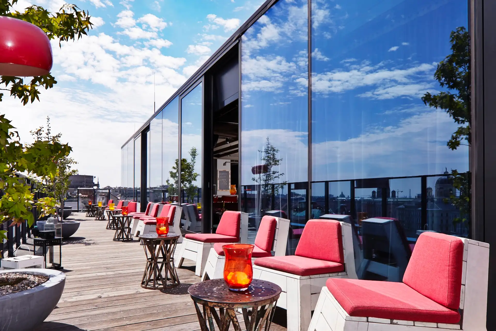 Dachterrasse mit Reihen roter Liegestühle und kleiner Tische mit Blick auf die Skyline der Stadt.