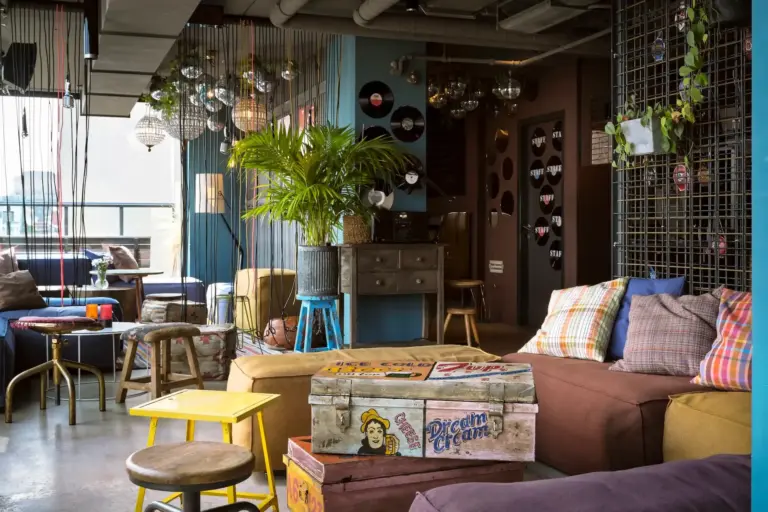Ein vielseitiger Loungebereich mit einem Stapel Vintage-Koffern als Couchtisch, niedrigen modularen Sitzmöbeln, einer Topfpalme und hängenden Pendelleuchten.