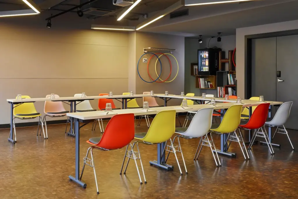 Ein U-förmiger Konferenztisch, umgeben von bunten Kunststoffstühlen, in einem modernen Besprechungsraum.