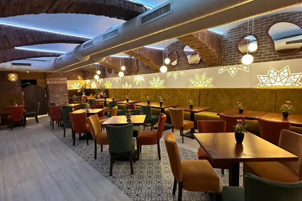 Die moderne Inneneinrichtung des Restaurants besticht durch Ziegelbögen, dekorative sternförmige Wandleuchten, Holztische und farbenfrohe Polsterstühle. Der Raum ist hell beleuchtet und strahlt eine gemütliche, einladende Atmosphäre aus.