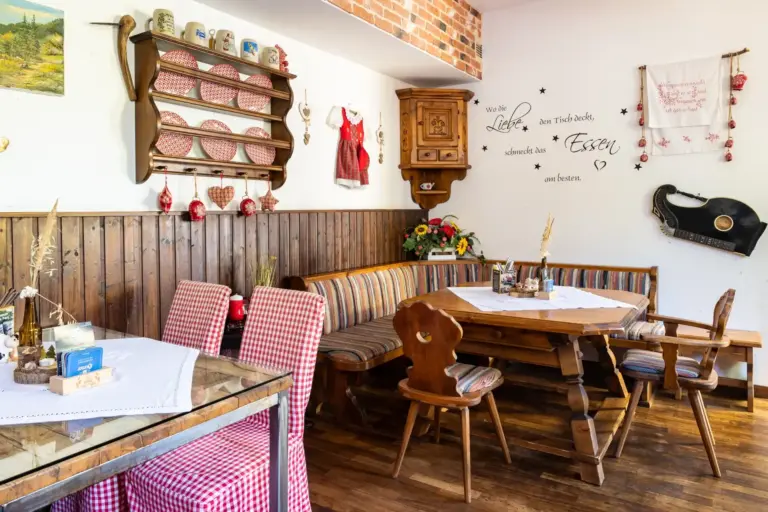 Ein gemütlicher, rustikaler Essbereich mit Holzmöbeln, karierten Tischtüchern und dekorativen Gegenständen an den Wänden, darunter eine Gitarre, Tassen, Blumen und Wandkunst. Eine Bank umgibt einen Ecktisch.
