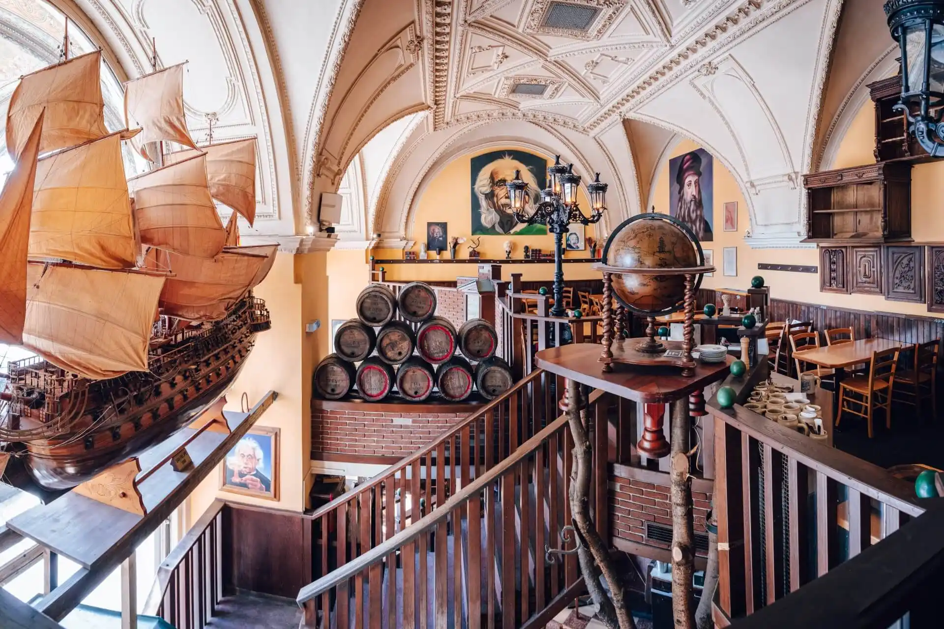 Das Restaurant ist mit einem großen Schiffsmodell, einem alten Globus, Weinfässern, einer Holztreppe, einer gewölbten Decke und Porträts von Entdeckern an den Wänden ausgestattet. Tische und Stühle sind überall im Raum verteilt.