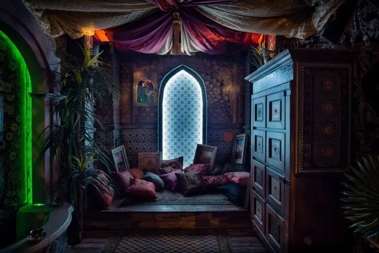 EscapeGame Kufstein Aufwendig dekoriertes Zimmer mit gemusterten Wänden, verzierten Bogenfenstern, Samtkissen, gerahmter Kunst, Pflanzen, einem großen Holzschrank und einer drapierten Stoffdecke, die eine gemütliche, exotische, vom Nahen Osten inspirierte Atmosphäre schaffen.