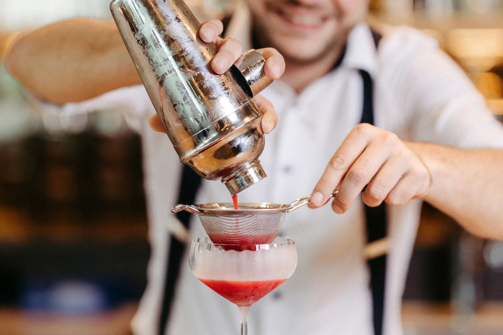Ein Barkeeper gießt einen leuchtend roten Cocktail durch ein Sieb in ein Glas.