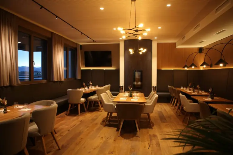Ein moderner Speisesaal eines Restaurants mit Holzböden, mehreren für das Abendessen gedeckten Tischen und modernen Leuchten.