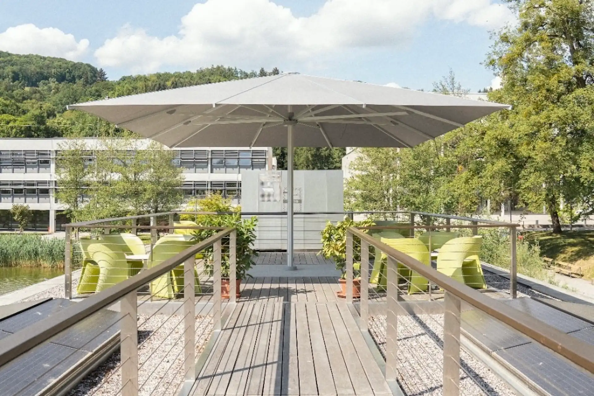 Terrasse im Freien mit einem großen grauen Sonnenschirm, der die limettengrünen Stühle auf einer Holzterrasse beschattet.