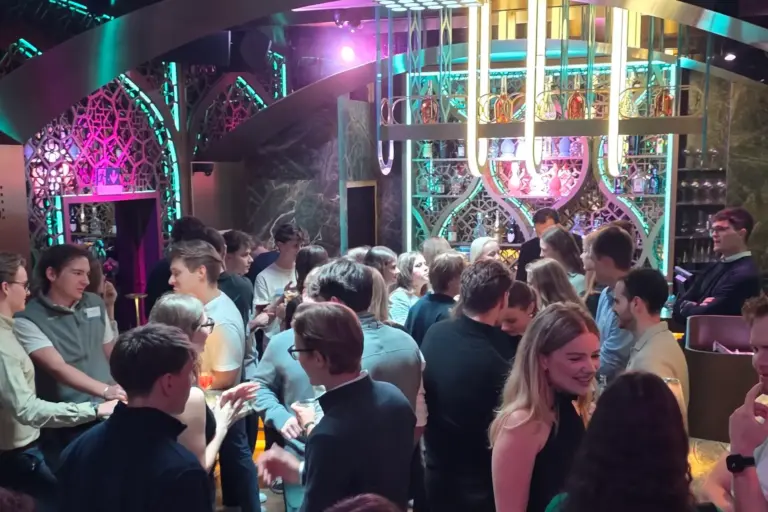 Eine lebhafte Gruppe junger Erwachsener trifft sich in einer lebhaften, modernen Bar mit bunter Beleuchtung und dekorativen Tafeln. Einige Leute unterhalten sich in Gruppen, während andere an der stylischen Bar stehen.
