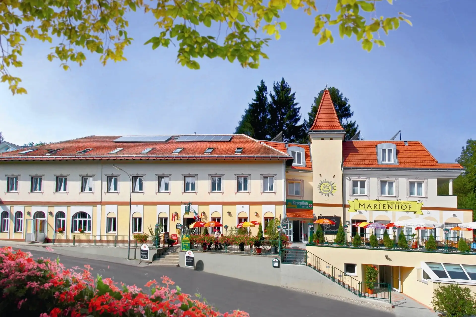 Das Gebäude des Hotels Marienhof mit einer Außenterrasse und einem Emblem mit Sonnenmotiv an der Außenwand.