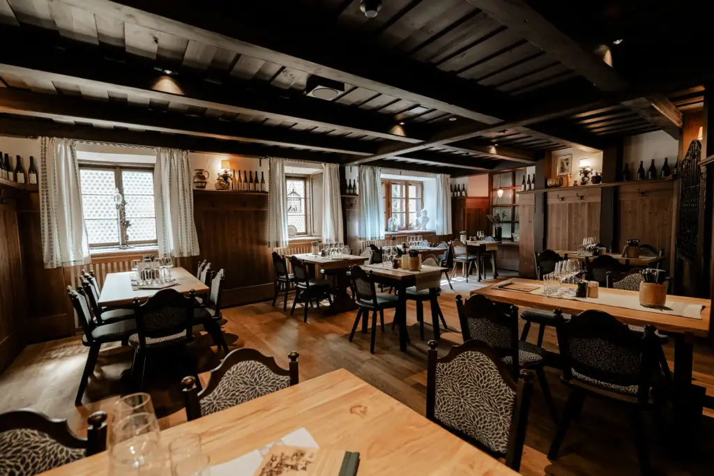 Ein gemütlicher, rustikaler Speisesaal mit Holztischen und -stühlen, Holzböden und -wänden, ordentlich eingedeckten Tischen mit Gläsern und natürlichem Licht, das durch vorgehängte Fenster fällt.