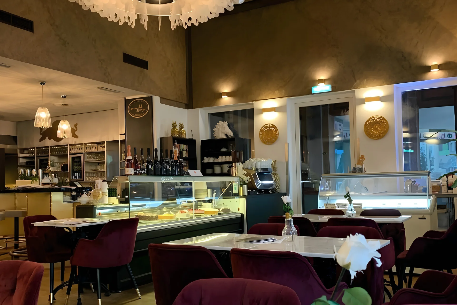 Mocca Lounge Das Interieur eines Cafés mit Tischen mit Marmorplatten, bequemen burgunderroten Stühlen und Glasvitrinen, in denen Kuchen ausgestellt sind.