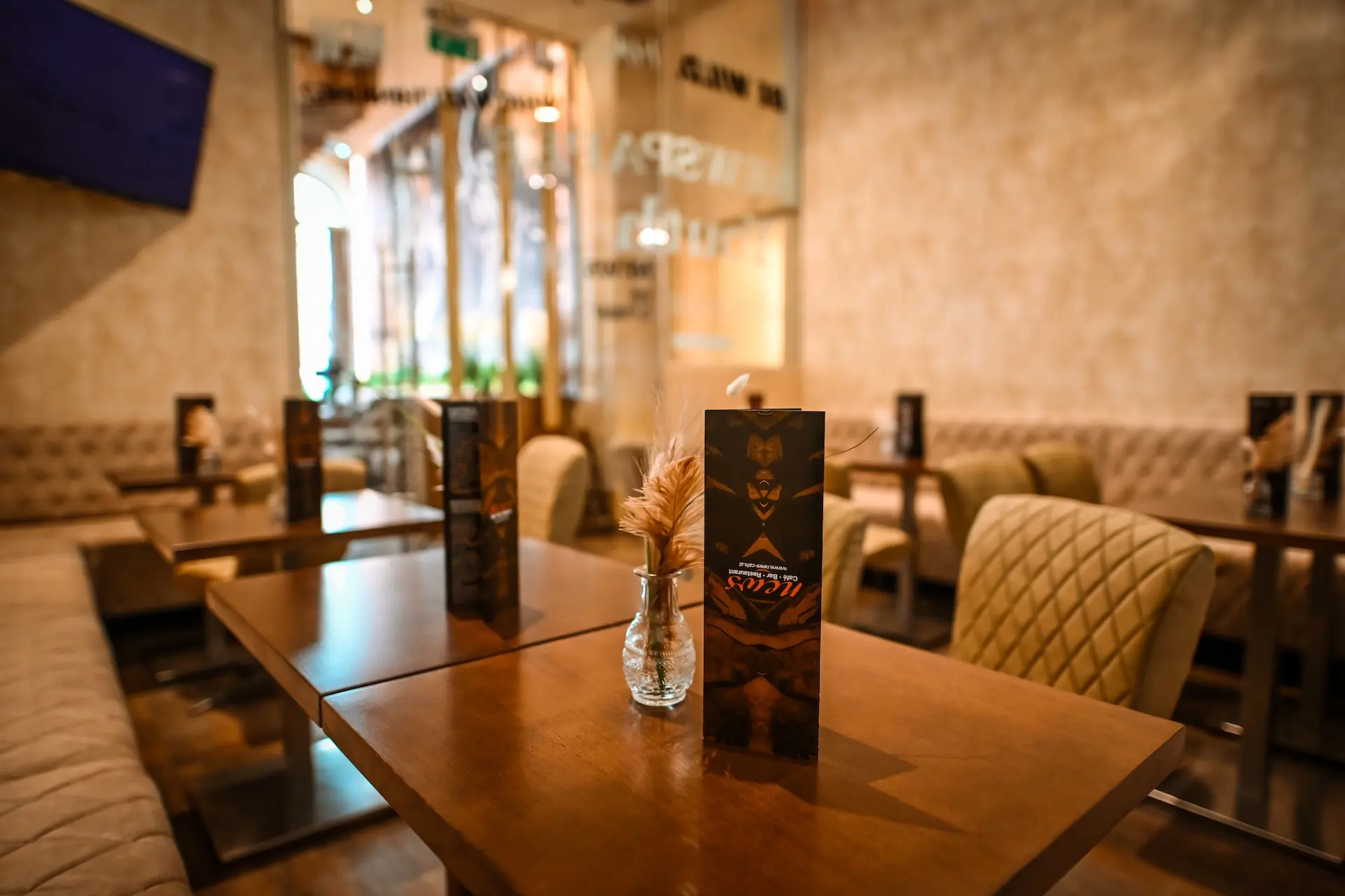 Ein gemütliches Restaurant mit Holztischen, beigen Steppstühlen und kleinen Vasen mit Trockenblumen. Die Speisekarten liegen auf jedem Tisch, und die warme Beleuchtung schafft eine einladende Atmosphäre.