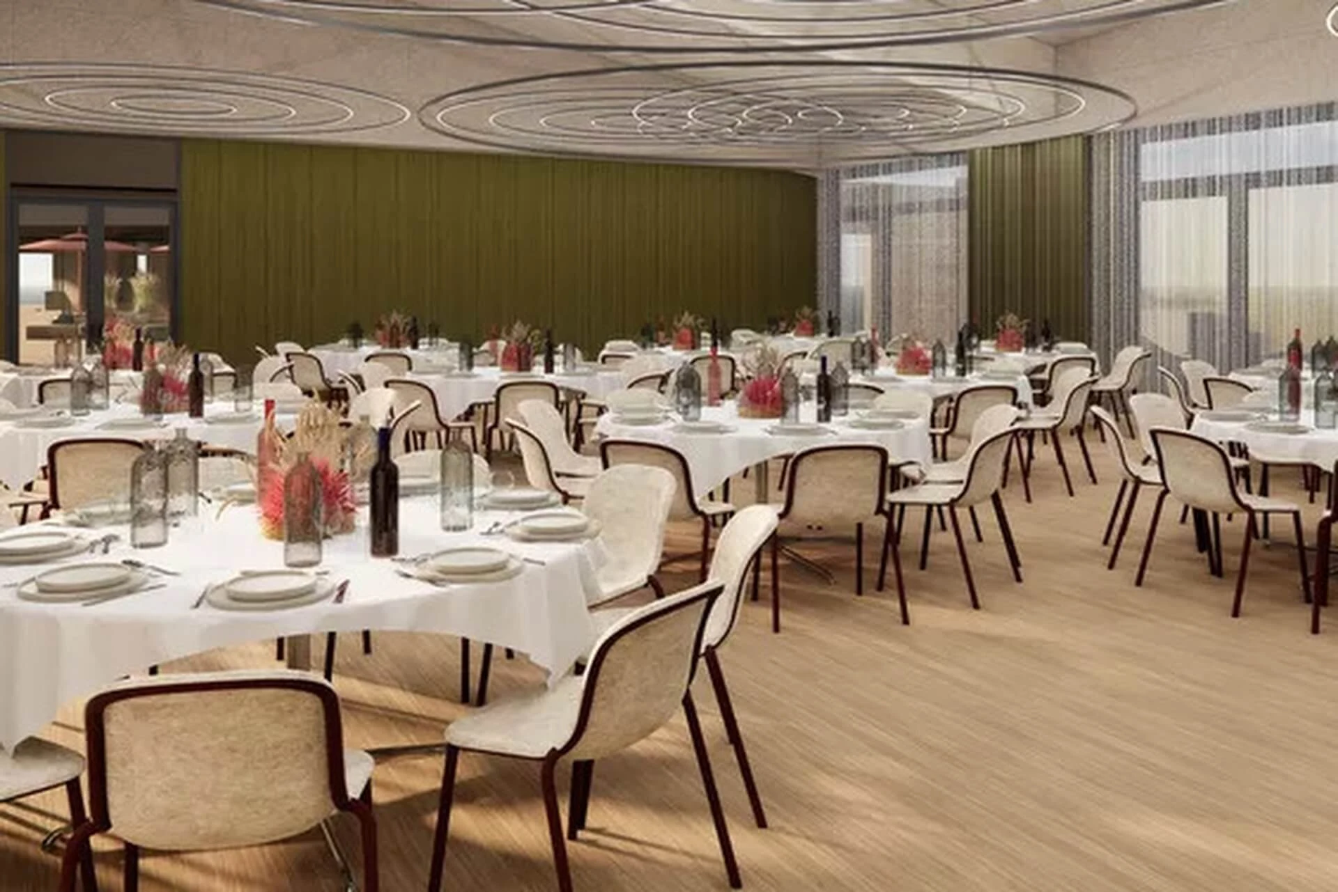 Ein moderner Bankettsaal mit runden Tischen, die mit Flaschen, Gläsern und Blumensträußen dekoriert sind. Cremefarbene Stühle umgeben die Tische, und große Fenster lassen natürliches Licht herein.