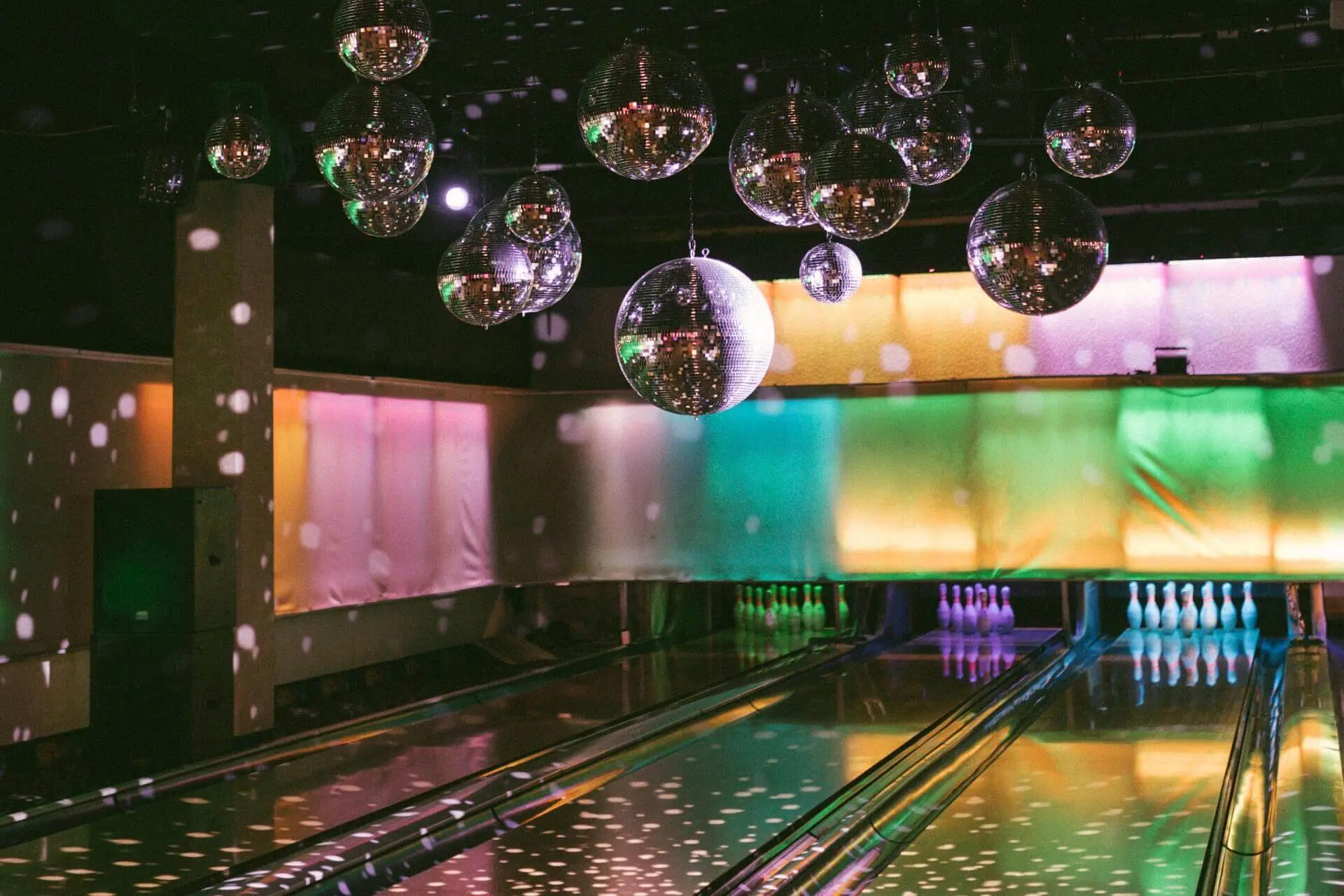 Mit bunten Lichtern beleuchtete Bowlingbahnen, beleuchtete Kegel und mehrere von der Decke hängende Discokugeln, die im ganzen Raum funkelnde Reflexe werfen.