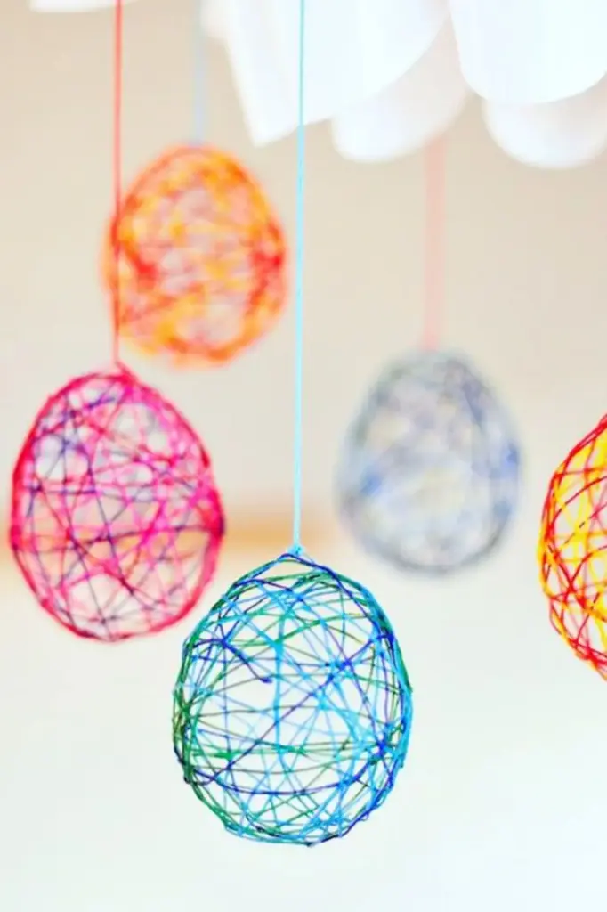 Bunte Garnkugeln hängen an Schnüren von der Decke herab. Perfekt für Osterdeko Basteln, jeder Ball ist aus verflochtenem Garn in leuchtenden Farben, die Schaffung einer dekorativen und spielerischen Display vor einem hellen Hintergrund.