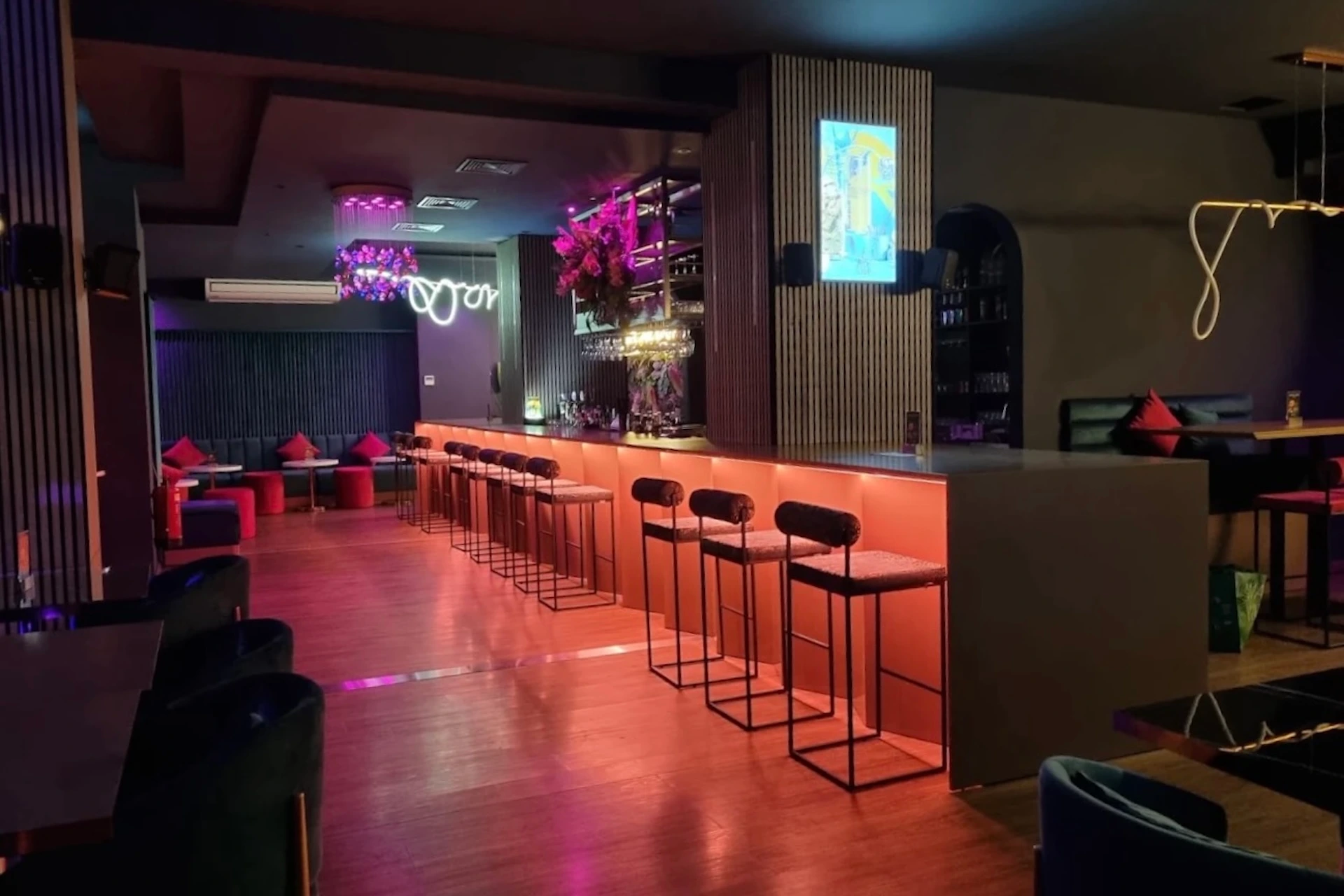 Eine moderne Bar-Einrichtung mit einer langen Theke, hohen Barhockern und rosa Akzentbeleuchtung.