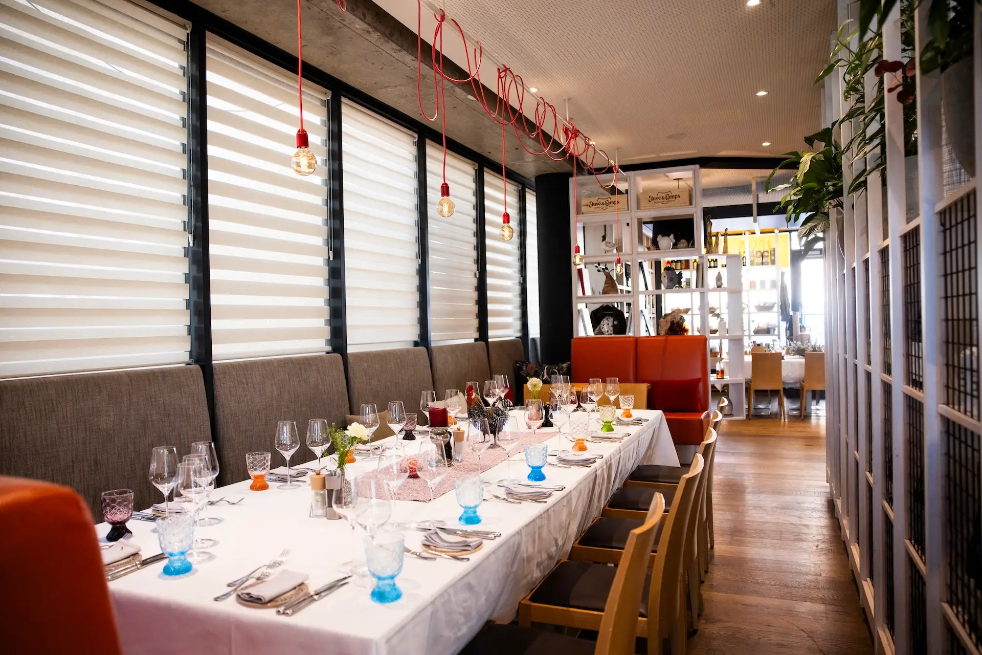 Ein langer Esstisch, gedeckt für ein festliches Essen mit weißen Tischdecken und buntem Glasgeschirr in einem modernen Restaurant.