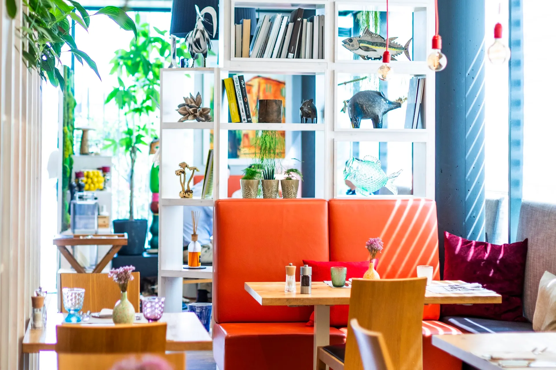 Orangefarbene Sitzbänke in einem Restaurant mit einem weißen Regal, das mit Büchern und Fischfiguren dekoriert ist.