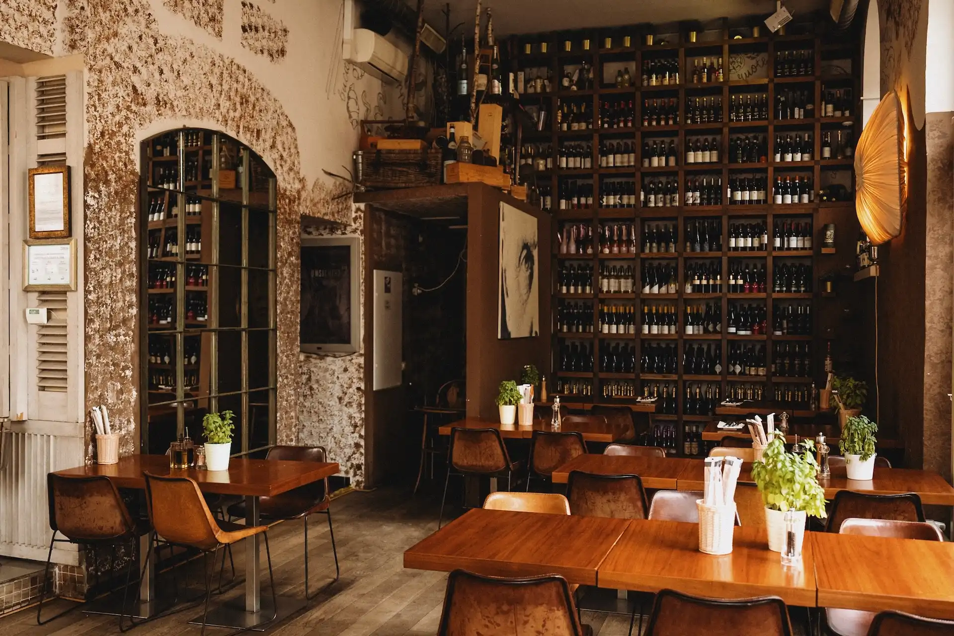 Innenansicht eines Restaurants mit Holztischen, braunen Lederstühlen und einem raumhohen Weinregal, das die Rückwand bedeckt.