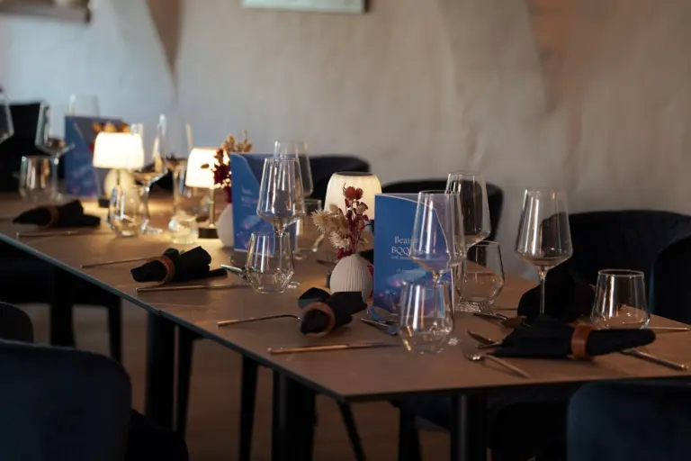 Ein langer Restauranttisch, gedeckt für das Abendessen mit Weingläsern, schwarzen Servietten, kleinen Tischlampen und Speisekarten für eine Feier am 23. September.