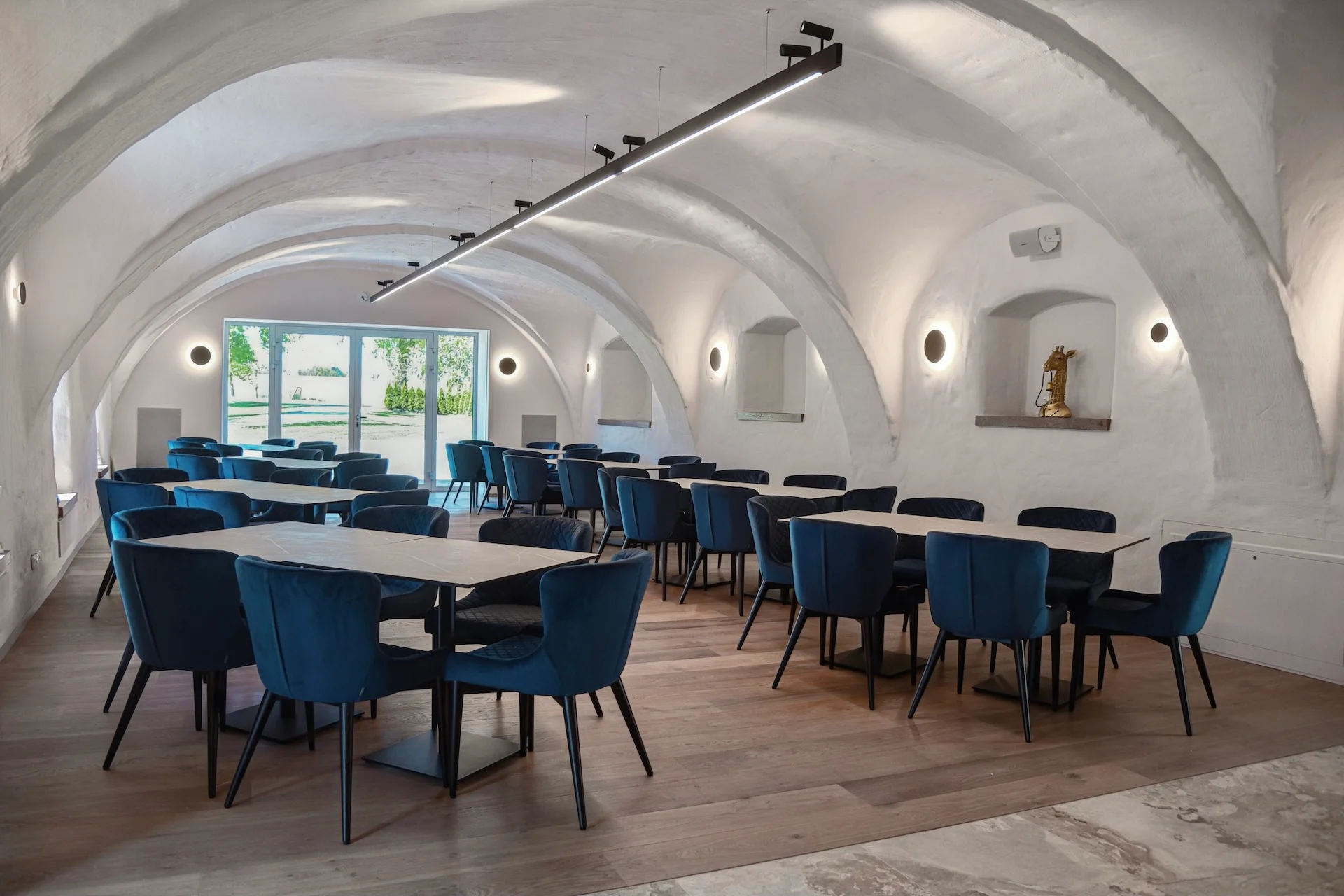 Speisesaal mit weißen Gewölbedecken, Holzböden und Tischreihen mit blau gepolsterten Stühlen.