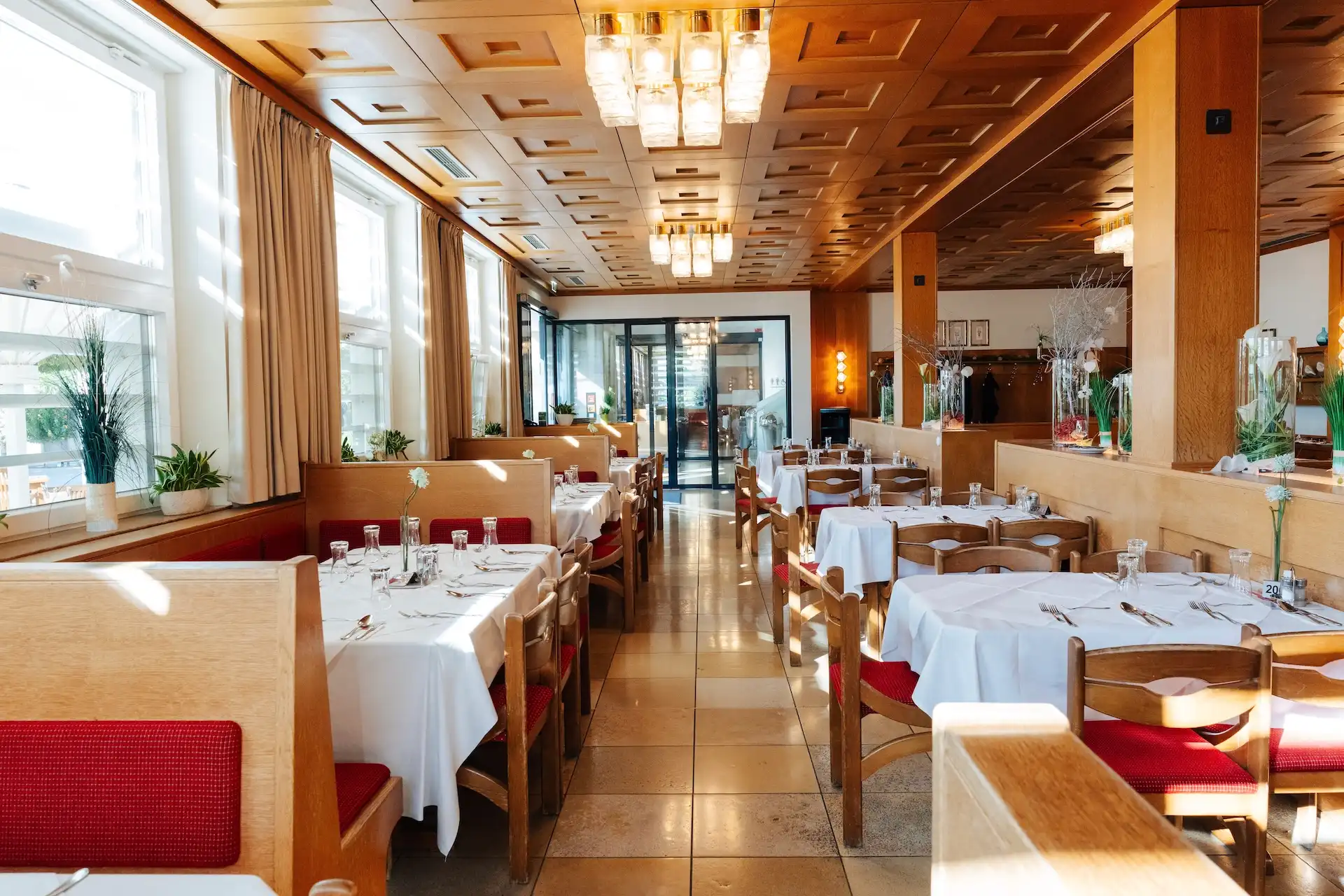 Reihen von Esstischen mit weißen Tischdecken und roten Stühlen in einem Restaurant mit holzgetäfelten Decken.