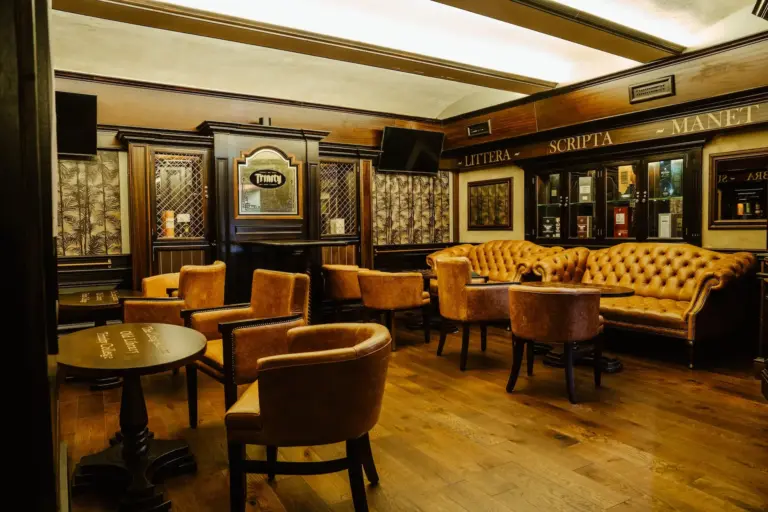 Eine gemütliche, gehobene Lounge mit braunen Ledersesseln und -sofas, Holztischen, polierten Holzböden und dunkler Holzvertäfelung, die eine warme und einladende Atmosphäre schafft.