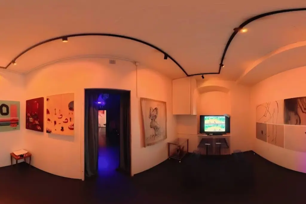 In einem warm beleuchteten Galerieraum sind verschiedene abstrakte Gemälde an weißen Wänden zu sehen; in der Mitte steht ein Fernseher, der ein buntes Bild zeigt. Eine dunkle Tür führt zu einem weiteren Raum mit violetter Beleuchtung.