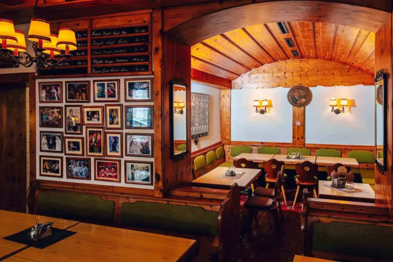 Ein gemütliches Restaurant mit hölzernen Wänden und Decken, grün gepolsterten Sitzgelegenheiten, gerahmten Fotos an der Wand und mehreren Tischen, an denen bei sanfter, warmer Beleuchtung gegessen wird.