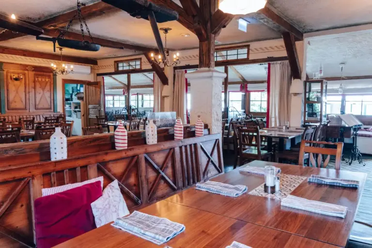 Ein gemütliches Restaurant mit Holztischen und -stühlen, gestreiften Servietten, dekorativen Mini-Leuchttürmen an einer Trennwand, freiliegenden Balken und großen Fenstern, die viel Tageslicht hereinlassen.