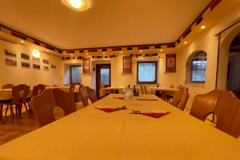 Ein gut beleuchteter Speisesaal mit Holzstühlen und Tischen mit gelben Tischtüchern, roten Servietten und rotem Besteck. Buntes Dekor und gerahmte Bilder schmücken die cremefarbenen Wände.